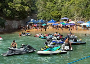 Grupo de jet skis navegando próximo à Ilha do Francês, em Macaé, com vegetação tropical e formações rochosas ao fundo